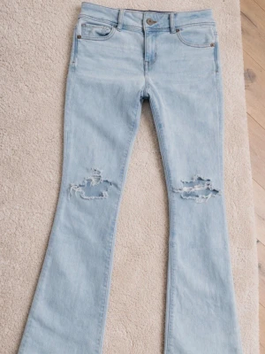 Ljusblå bootcut jeans med slitningar - Assnygga ljusblå bootcutjeans från american eagle. Dem är lågmidjade och har slitningar på knäna. De har en klassisk femfickmodell och är perfekt för en snygg avslappnad look.💕🩵🌟