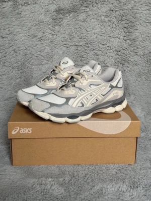ASICS grå och vita sneakers - Snygga sneakers från ASICS i grått och vitt med beige detaljer. Ovandelen är i mesh och mocka för en sportig vibe och bra andningsförmåga. Klassisk ASICS-logga på sidan och bekväm, dämpad sula. Perfekta för dig som gillar stilrena och trendiga skor.