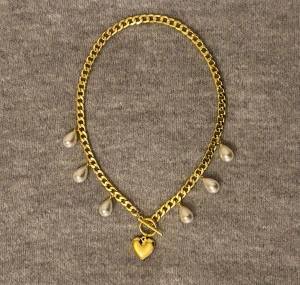 Guldigt halsband med pärldroppar - Snyggt halsband i guldfärgad metall med fem hängande pärldroppar och ett hjärtformat hänge framtill. Kedjan är chunky och ger ett trendigt intryck. Perfekt accessoar för att lyfta din outfit. Nytt skick 