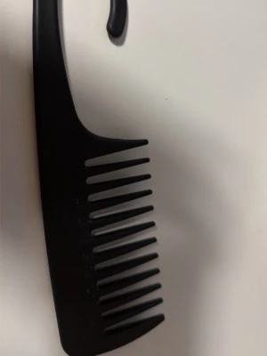 Svart bredtandad kam i plast - En svart bredtandad kam i plast med ett praktiskt handtag. Perfekt för att reda ut håret utan att slita, särskilt för lockigt eller tjockt hår. Enkel och stilren design som passar i väskan eller badrummet.