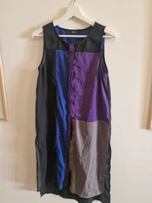 Färgstark ärmlös klänning zoul Edition - Unik ärmlös klänning från Zoul Edition i färgblock med svart, blå, lila och grå. Rak passform med knappar framtill och rund halsringning. Perfekt för dig som gillar statement-plagg och vill sticka ut med en cool och modern look.