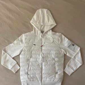 Moncler, Vit Cardigan - Vit Moncler cardigan strlk. M Herr Använts väldigt få gånger förra sommaren, sedan dess har den legat i min garderob.  Måtten på jackan är: Längd 66cm Byst 56cm Axlar 49cm Ärmar 67cm 