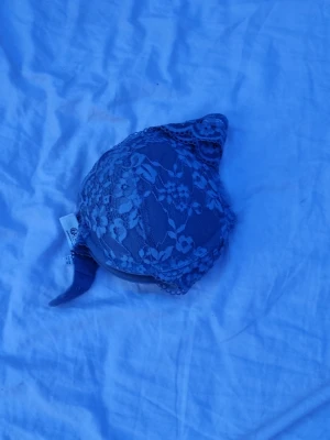 Blommig spets-bh i blått - Snygg bh i blå spets med blommigt mönster och vadderade kupor. Axelbanden är justerbara och bh:n har hakknäppning bak. Perfekt för dig som gillar romantiska detaljer och en feminin look.