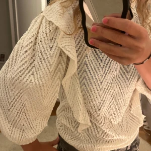 Vit spetsblus med volang från MNG - Supersöt vit spetsblus från Mango med zigzag-mönster och volangdetaljer på axlarna. Blusen har långärmade puffärmar. Perfekt för en snygg look! Den är i M men  passar mer s/xs så den är alltså lite mindre i storleken.💓som ni ser på bilden så är lappen med storlek o märket på av på ena sidan men det är inget som spelar roll då man bara kan klippa bort den!