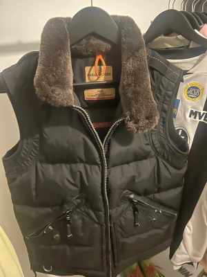 Svart dunväst från Parajumpers - Säljer en svart dunväst från Parajumpers med hög krage och mjukt foder. Västen har två snedställda dragkedjefickor framtill och detaljer i metall. Perfekt för lager-på-lager och riktigt snygg till höst- och vinterlooken.