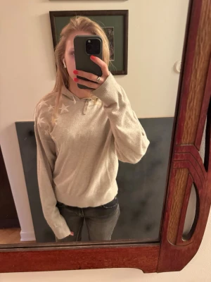 Beige stickad hoodie med stjärnor - Snygg beige hoodie med vita stjärnor på axeln och en stor stjärna på ryggen. Hoodien har huva och ribbade muddar vid ärmslut och midja. Perfekt för en avslappnad och trendig look. Väldigt Mjuk och skön, passar till jeans eller leggings. 