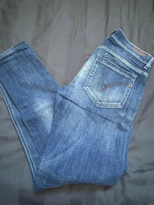 Blå jeans från Dondup - Säljer ett par klassiska blå jeans från Dondup med snygg tvätt och raka ben. Jeansen har fem fickor, silverfärgade nitar och en läderpatch med logga bak i midjan. Materialet är slitstark denim i bomull. Perfekta för en avslappnad och trendig look.