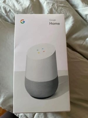 Google Home smart högtalare vit - Google Home är en smart trådlös högtalare i vit och ljusgrå färg med minimalistisk design. Den har röststyrning via Google Assistant och stöd för Spotify, Netflix, YouTube och Philips Hue. Perfekt för att styra smarta hemmet och spela musik trådlöst.