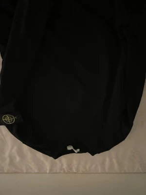 Svart hoodie från Stone Island - Säljer en svart hoodie från Stone Island med den klassiska loggan på vänster ärm. Hoodien har en enkel och clean design, perfekt för dig som gillar streetwear. Tillverkad i mjukt bomullsmaterial för skön komfort.