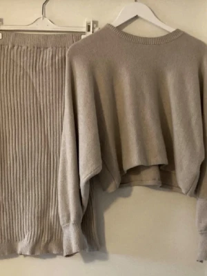 Beige ribbad kjol i stickat material - Trendig beige kjol i stickat material med ribbad struktur. Kjolen har en rak passform och resår i midjan för extra komfort. Perfekt att matcha med en stickad tröja för en avslappnad men stilren look.