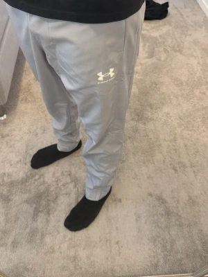 Grå mjukisbyxor från Under Armour - Snygga grå mjukisbyxor från Under Armour med logga på vänster lår. Byxorna har en rak passform och är tillverkade i ett mjukt och lätt material som känns skönt mot huden. Perfekta för chill eller träning. Använda 2 gånger