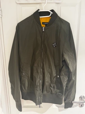 Olivgrön bomberjacka från J.Lindeberg - Säljer en riktigt snygg bomberjacka från J lindberg i ett reflekterande material. Den har bara använts 1 gång så den är så gott som ny. Strl är M. Bara att höra av sig vid minsta lilla