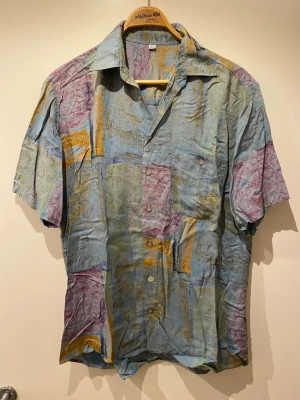 Färgglad kortärmad skjorta i bomull - Säljer en unik kortärmad skjorta med abstrakt mönster i blått, grönt, gult och lila. Storlek M men passar lite mer som L. 