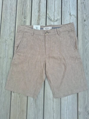 Nya Linneshorts från Dressmann, strl XS - Säljer ett helt nytt par beigea shorts från Dressmann i linne. Klassisk passform, fickor fram och bak samt bälteshällor och knappstängning. Nypris 499 kr