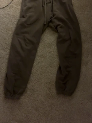 Bruna Essentials mjukisbyxor - Säljer ett par bruna mjukisbyxor från Essentials Fear of God i storlek M. Byxorna har resår i midjan och benslut, samt sidofickor. Materialet är mjukt och bekvämt, perfekt för chill dagar. Diskret logga på benet.