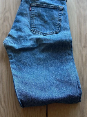 Blå Levi's raka jeans - Klassiska blå jeans från Levi's med rak passform och fem fickor. Jeansen har en tydlig bakficka med den ikoniska röda Levi's-lappen och är gjorda i slitstark denim. Perfekta för en avslappnad och tidlös stil.