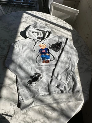 Grå hoodie Polo Bear Ralph Lauren - Snygg och bekväm  Ralph Lauren bear hoodie. Aldrig använd. 550kr. Storlek S