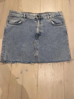 Blå jeanskjol med rå kant - Snygg blå jeanskjol i klassisk modell med rå, fransig kant nertill och femficksdesign. Kjolen har bälteshällor och dragkedja framtill. Perfekt för dig som gillar en avslappnad och trendig stil.