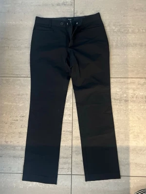 Svarta kostymbyxor från Filippa K - Stilrena svarta kostymbyxor från Filippa K med raka ben och klassisk passform. Byxorna har hällor för skärp, diskreta sidofickor och stängs med knapp och dragkedja. Perfekta för en clean och snygg look. Ca storlek 50