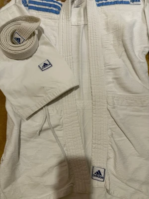 Vit karate från Adidas - Karatekläder från Adidas i vitt med ljusblå ränder på axlarna och Adidas-logga på jacka, byxa och bälte. Klassisk design med förstärkta sömmar och traditionellt bälte.