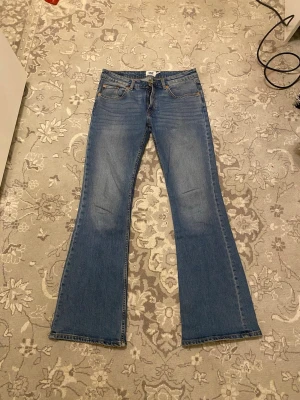 Blå bootcut jeans  - Säljer ett par klassiska blå bootcut jeans från med femficksdesign och snygga slitningar på framsidan. Jeansen har normal midja och är tillverkade i denim med stretch för extra komfort. Perfekt för dig som gillar retrostil och vill ha ett par jeans med utsvängda ben.