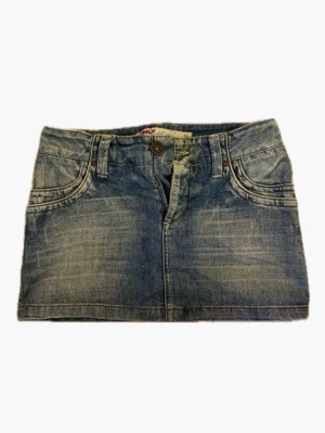 Blå lågmidjad jeanskjol från Only - Säljer en klassisk blå jeanskjol från Only med femficksdesign, knapp och dragkedja framtill samt snygga bakfickor. Kjolen har en kort passform och är tillverkad i slitstarkt denim-material. 