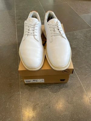 Vita sneakers från Puma i läder - Stilrena vita sneakers från Puma med klassisk låg profil och snörning. Skorna är tillverkade i slätt läder med diskret Puma-logga på plösen. Yttersulan är vit med en beige kant som ger en clean look. Perfekta för dig som gillar minimalistisk och fräsch stil. Skon har används max 10 tal gånger så i princip helt nya. Bara skriva om de är några frågor😁