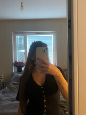 Svart v-ringad topp med knappar - Snygg svart topp från Gina Tricot med v-ringning och korta ärmar, som tyvärr aldrig kom till användning. Toppen har en rad med dekorativa knappar framtill och är figurnära i modellen. Perfekt att styla med jeans eller kjol för en trendig look.