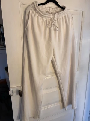 Vita mjukisbyxor med dragsko Lager157 - Säljer ett par vita mjukisbyxor med bred resår i midjan och dragsko för perfekt passform från Lager157. Byxorna har raka ben och sidofickor. Perfekta för chill dagar eller när du vill vara extra bekväm. Materialet känns mjukt och skönt mot huden.