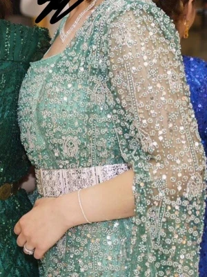 Grön glittrig långklänning med bälte - Säljer en elegant grön kurdisk klänning med glittriga paljettdetaljer och transparenta ärmar. Klänningen har ett brett och ett vackert mönster över hela tyget. Klänningen är fylld av paljetter och väger 4 kg