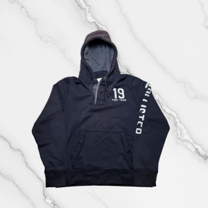 Vintage Hollister hoodie - herr strl XL - Säljer en vintage Hollister hoodie i svart färg i storlek XL med dubbel knappkrage. Hollister brodering över vänster ärm samt 19 Surf Team brodering på vänster sida av bröstkorgen.  👕 Märke: Hollister 📏 Storlek: XL 🎨 Färg: Svart, sol faded luva 🧵 Material: 70% bomull, 30% polyester 📐 Mått: 69 cm lång, 60 cm bred 📌 Skick: Bra skick, liten skada nedtill på vänster ärm (se bilder)  💬 Hör av dig vid frågor 💰 Pris kan diskuteras vid snabb affär 📦 Skickas inom 24 timmar