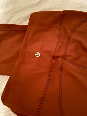 Bruna leggings från Lululemon - Säljer ett par snygga bruna leggings från Lululemon med hög midja och synliga sömmar. Helt oanvända har inte ens provat ännu. 