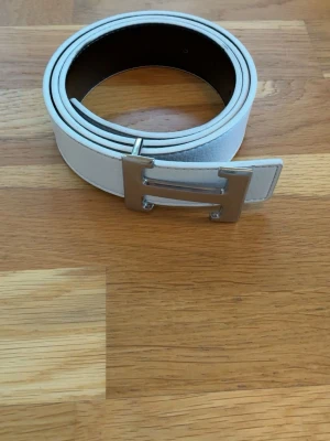 Vändbart bälte med silverfärgat H-spänne - Snyggt vändbart bälte i svart och vitt läder med ikoniskt silverfärgat H-spänne. Perfekt assessor för att lyfta vilken outfit som helst klassisk design med exklusiv känsla och justerbara hål för bästa passform. Bältet är 110cm långt. Säljer för 249kr men är öppen för prisförslag, skickar inom en dag.