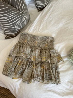 Mönstrad volangkjol strl M - Kort volangkjol i beige och bruna toner med paisleyinspirerat mönster. Köpt i en boutique i karibien, jättefint men knappt använd så den är i nyskick! 