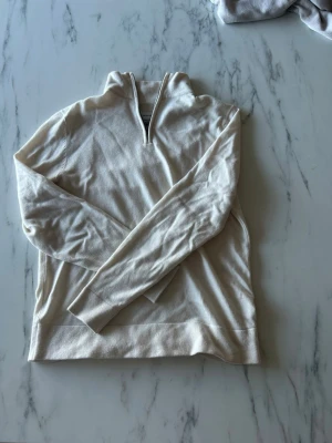 Beige merinoulltröja från These Glory Days - Snygg beige stickad tröja från These Glory Days i mjuk merinoull. Tröjan har halv dragkedja vid halsen och långa ärmar. Perfekt för lager-på-lager och enkel att matcha med andra plagg. Använd fåtal gånger.