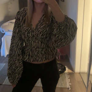 Zebramönstrad blus med ballongärm - Säljer en trendig zebramönstrad blus med v-ringning och vida ballongärmar. Blusen har smock i midjan för en snygg passform och är i ett lätt, vävt material. Tröjan är helt slutsåld🦓💕