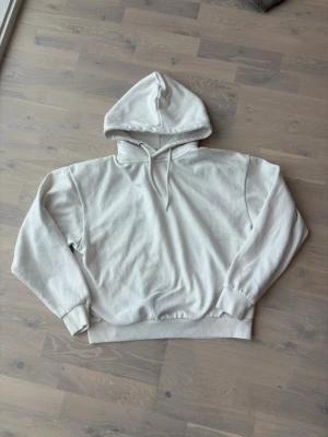 Vit oversized hoodie - En stilren Vit hoodie med huva och dragsko. Hoodien har en relaxed, oversized passform och ribbade muddar vid ärmar och midja. Tillverkad i mjukt bomullsmaterial som känns skönt mot huden. Perfekt för en chill och avslappnad look.