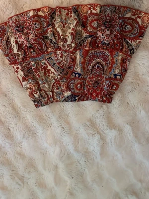 Mönstrad kortkjol i boho-stil - Säljer en färgstark kortkjol med bohemiskt mönster i rött, blått, beige och vitt. Kjolen har volangdetaljer och elastisk midja för skön passform. Perfekt för dig som gillar statement-plagg och vill sticka ut med coola prints. ( jag köpte den i spanien för 3 år sen, så vet tyvärr inte storlek men skulle säga att den är som Xs-S) 