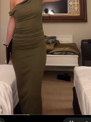 Olivgrön oneshoulder långklänning - Snygg olivgrön långklänning med oneshoulder-design och draperad överdel. Klänningen har en figurnära passform och är tillverkad i ett mjukt, stretchigt material som ger en smickrande siluett. Perfekt för dig som vill sticka ut med en unik och trendig look.