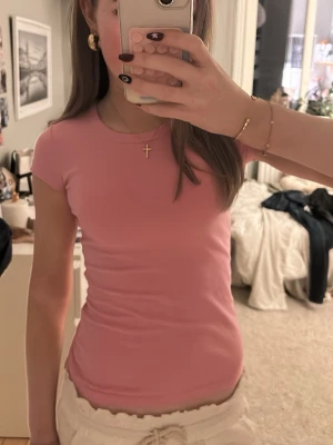 Söt rosa topp - Säljer en rosa söt topp med korta ärmar. T-shirten har en tight passform och är perfekt för en fin sommaroutift. Materialet är jätte mjukt och bekvämt.