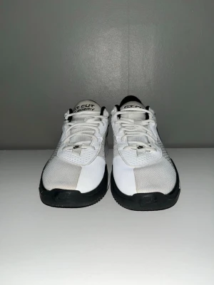 Nike vitt sneakers med svart detalj - Snygga vita Nike sneakers med svarta detaljer och meshpaneler för extra andningsförmåga. Modellen har lågt skaft, klassisk snörning och texten '001' på hälen. Perfekta för dig som gillar sportig och clean stil.