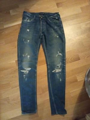 Blå slitna jeans från Dsquared2 - Säljer ett par blå jeans från Dsquared2 med slitningar och distressed detaljer på både fram- och baksida. Klassisk femficksmodell med knappgylf och raka ben. Perfekta för en avslappnad och trendig look. passar 175-190