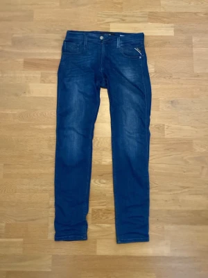 Blå slim fit jeans från Replay - Snygga blå slim fit jeans från Replay i storlek w29 L32 med klassisk femficksdesign och dragkedja fram. Jeansen har en lätt tvättad look och raka ben. Materialet är mjukt denim som ger en bekväm känsla och passar perfekt till en avslappnad stil. De är varsamt använda och fortfarande i bra skick. Pris kan diskuteras.