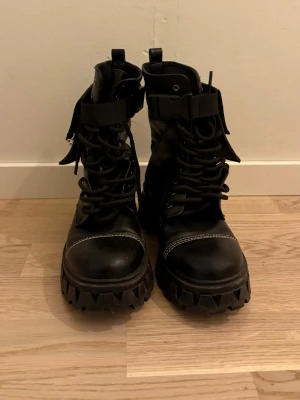 Svarta chunky boots med ficka - Svarta boots med grov sula, snörning och dragkedja på sidan. Dekorativ vit söm och en cool avtagbar ficka med textdetaljer på utsidan. Tillverkade i syntetmaterial med robust känsla och edgy stil.