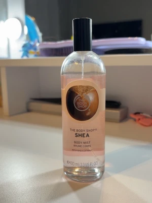 The Body Shop Shea Body Mist - Fräsch body mist från The Body Shop med shea-extrakt. Kommer i en genomskinlig glasflaska med svart plastlock och enkel sprayfunktion. Doften är mjuk och varm, perfekt för dig som gillar naturliga och krämiga toner. Flaskan rymmer 100 ml.
