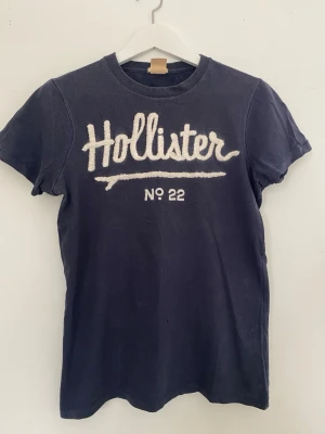 Vintage mörkblå Hollister t-shirt med tryck - Snygg mörkblå t-shirt från Hollister med vit broderad logga och texten 'No 22' framtill. Klassisk rund halsringning och korta ärmar. Perfekt för en avslappnad och trendig stil.
