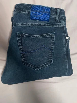 Jacob choen  - Snygga mörkblå skinny jeans med en unik blå patch med broderad logga bak i midjan. Jeansen har klassisk femficksdesign och kontrastsömmar på bakfickan. Tillverkade i stretchigt denim för en bekväm passform. Är storlek 36 men passar 34!