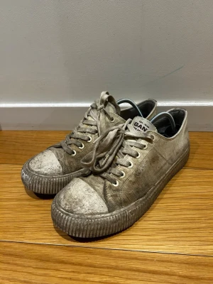 Gant sneakers *42* - Snygga beige sneakers från Gant med klassisk låg profil och vita snören. Skorna är tillverkade i canvas med gummisula och har en mörkbrun detalj på hälen. Perfekta för dig som gillar en enkel och stilren look.
