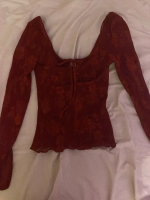 Vinröd långärmad topp med snörning - Vinröd långärmad topp från Gina tricot med blommigt mönster och snygg snörning framtill. Toppen har en croppad passform och djup urringning, perfekt för att lyfta din stil. Materialet är lätt och stretchigt.