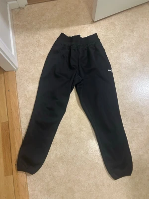 Svarta mjukisbyxor från Puma - Svarta mjukisbyxor från Puma med klassisk logga på låret. Byxorna har resår i midjan och vid bensluten för en skön passform. Perfekta för chill eller träning. Tillverkade i mjukt material som känns bekvämt hela dagen.